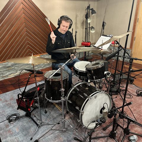Zach Danziger behind his drum kit in the studio, wearing headphones.