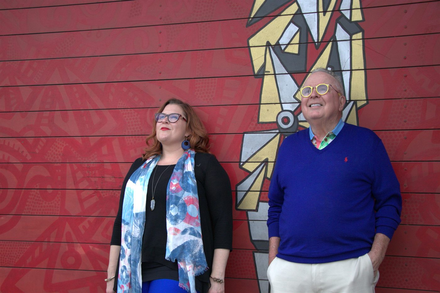 Jenn Quader and her father Dr. Dennis Michels standing against a red mural wall, both looking upward.