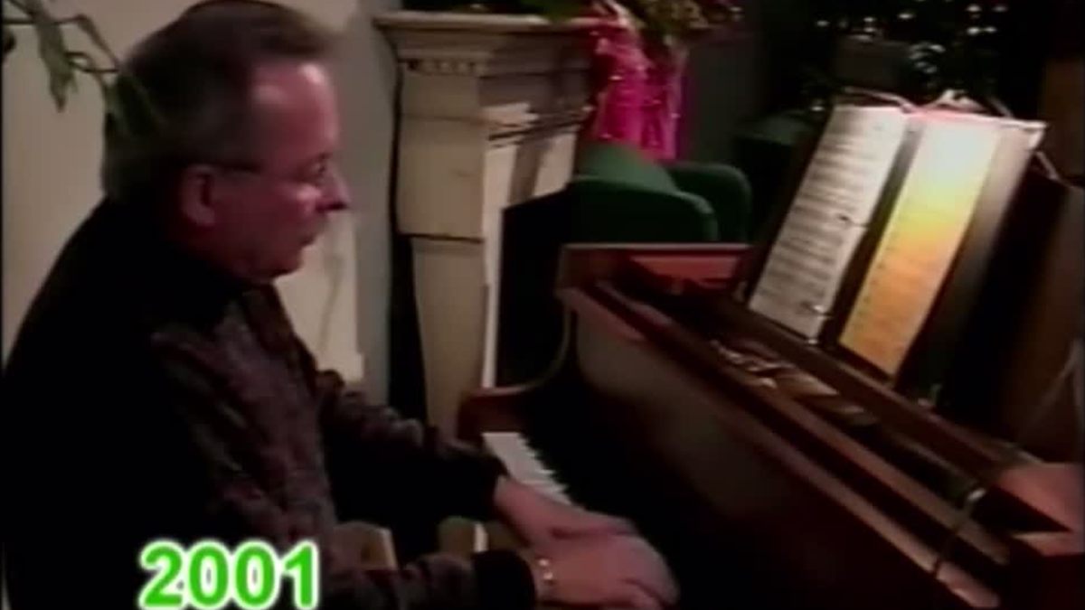 Dr. Dennis Michels playing the piano in a room decorated for Christmas, a frame from the 2001 Musical Michels Christmas Special.