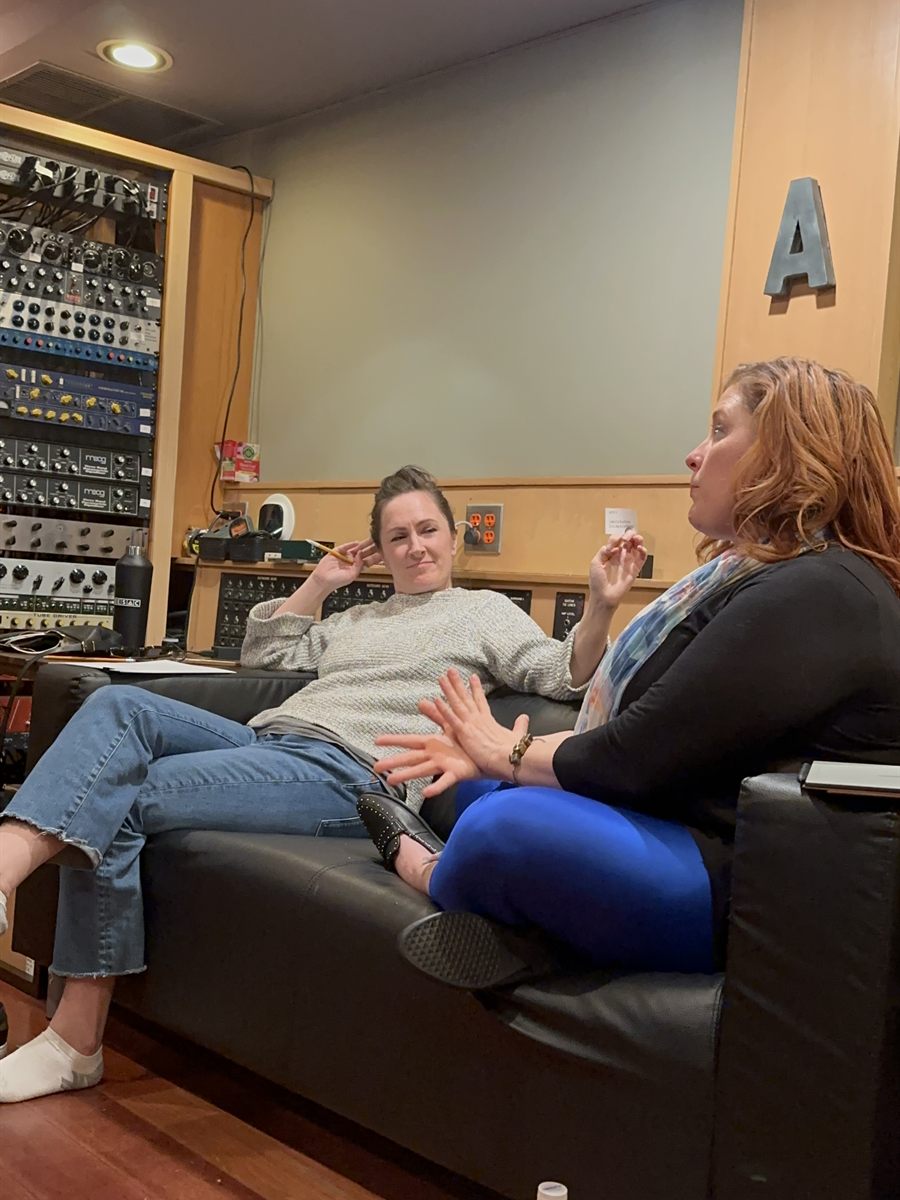 Sara Gazarek and Jenn Quader sitting together on the control-room couch at LMNL, mid-conversation, racks of outboard gear behind them.