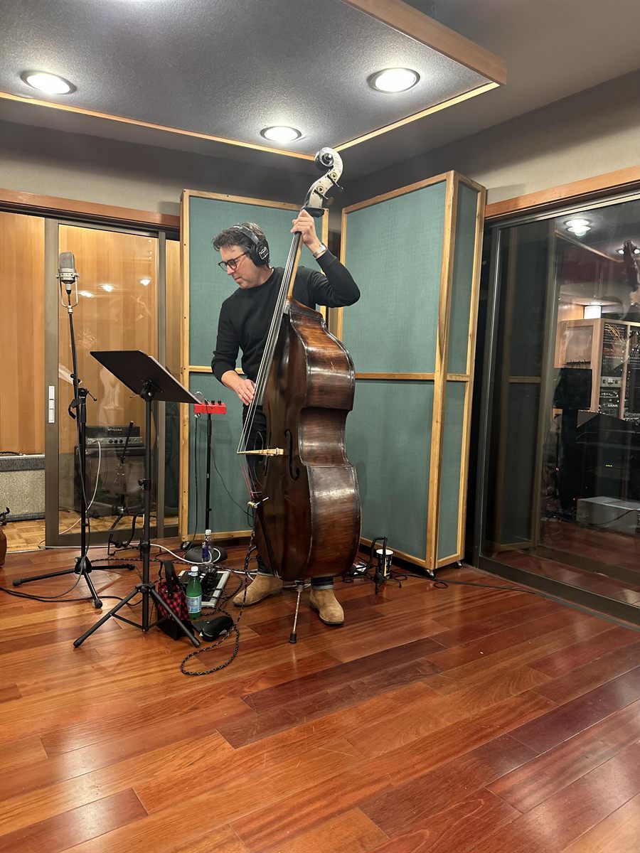 Sean Hurley standing with his upright bass in the LMNL live room, in headphones and a black polo neck.