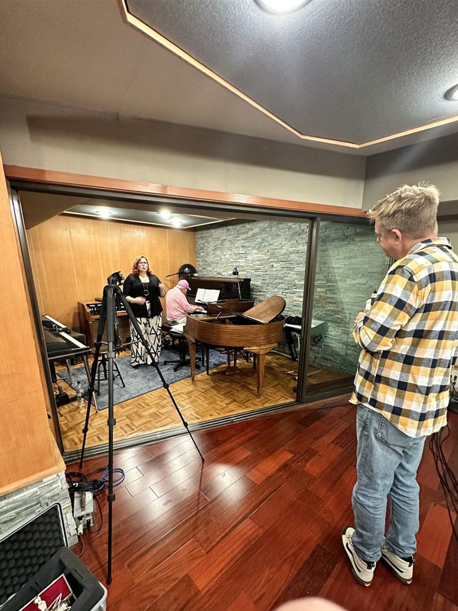 Seen from the control room through the glass: Jenn Quader singing while Dr. Dennis Michels plays the grand piano, with Jeff Babko standing in the foreground watching, arms folded.