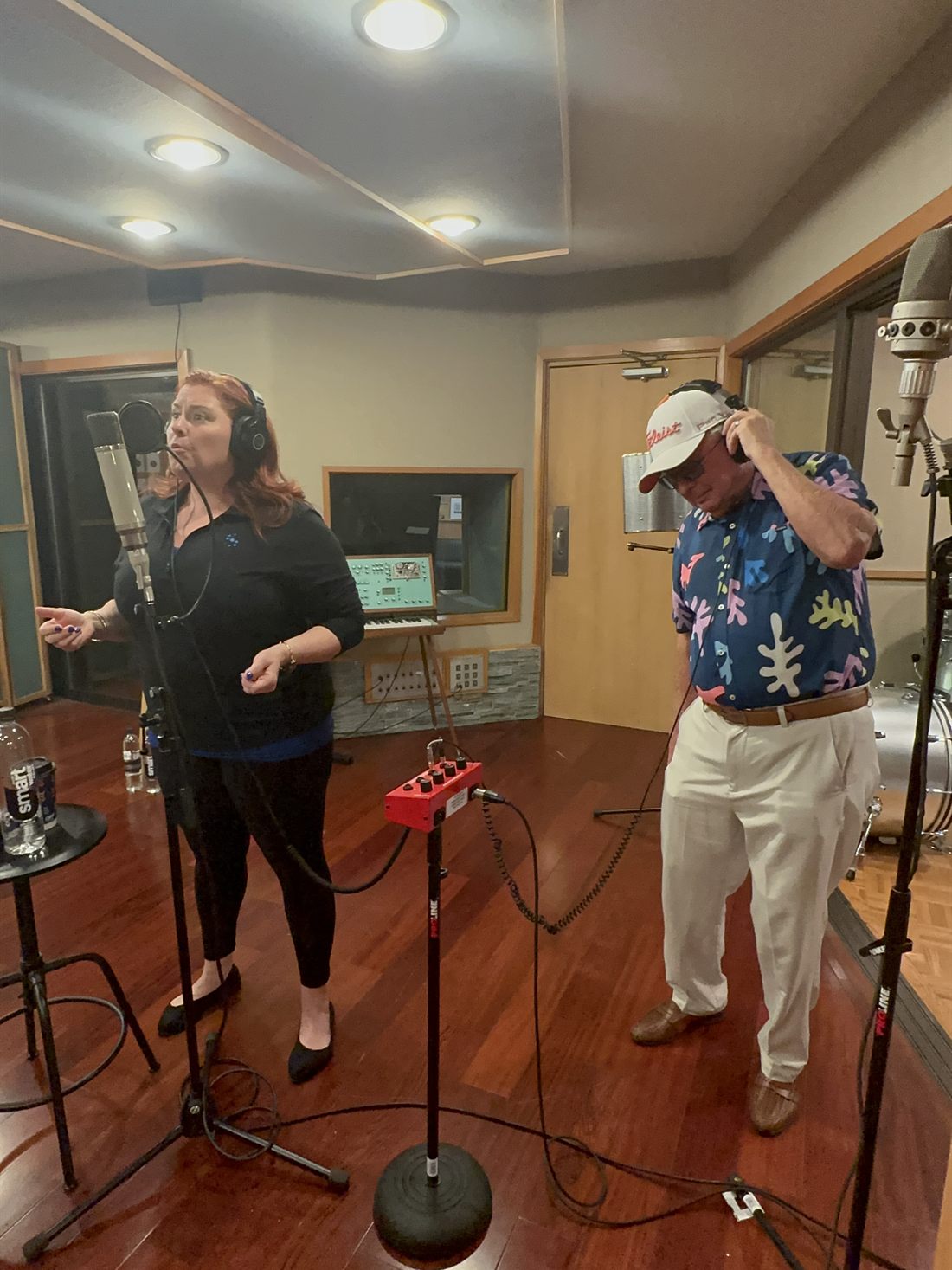 Jenn Quader singing into a condenser microphone in the live room while Dr. Dennis Michels stands a few feet away in headphones.